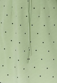 Vihreä kangas, jossa on pieniä mustia pilkkuja, ja jossa on nyöriyksitys sekä pehmeä rakenne. Sopii vapaa-ajan vaatteisiin.