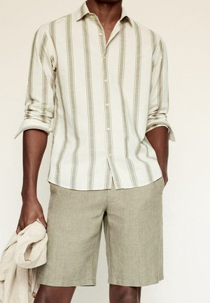 Camisa de botones con rayas claras en tonos beige y oliva, combinada con pantalones cortos de color oliva. La tela parece ligera y con textura.