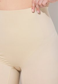 Leggings beige a vita alta con una texture liscia, caratterizzati da un design aderente e dettagli di cucitura discreti lungo i lati.