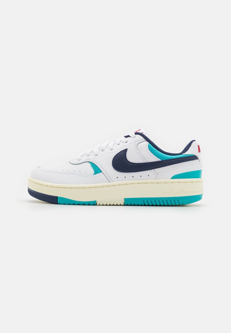 Basket basse blanche Nike avec un swoosh bleu marine, des accents bleu sarcelle, une semelle beige et un logo rouge au talon et sur la languette, vue de côté.