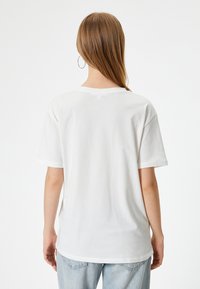 Hvid bomulds T-shirt med afslappet pasform, korte ærmer og ribbet rund hals, vist fra ryggen mod en ensfarvet baggrund.