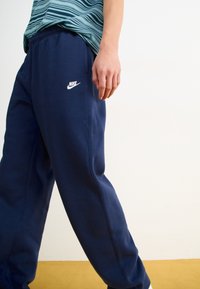 Σκούρες μπλε φόρμες από μαλακό ύφασμα, με ελαστική μέση, πλευρικές τσέπες και λευκό λογότυπο Nike στο αριστερό μηρό.