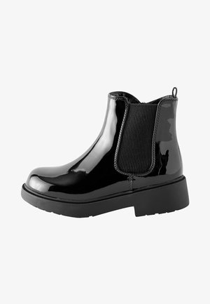 Botines de charol negro con paneles laterales elásticos y una lengüeta, que cuentan con una suela de goma negra gruesa y una textura suave y brillante.