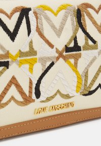 Bolso de tela crema con bordados de zigzag multicolores y el logo dorado "LOVE MOSCHINO" sobre un ribete de cuero marrón.