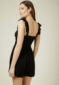 Combinaison noire avec des bretelles à volants, un buste smocké et un short ample. Le tissu semble doux avec une texture lisse.