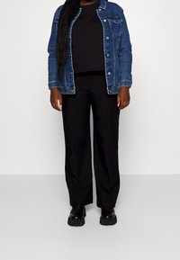 Jeansjacka i blå, bärs över en svart kort topp, kombinerad med svarta vida byxor och klumpiga svarta skor. Enkel, avslappnad outfit.