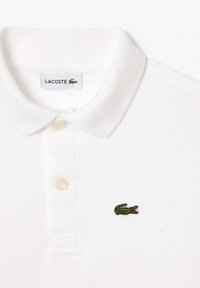 Polo blanc Lacoste avec col, deux boutons et petit logo crocodile vert brodé sur la poitrine.