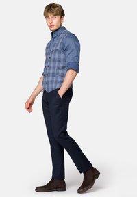 Niebieska kamizelka w kratę na ciemnoniebieskiej koszuli, połączona z ciemnymi spodniami i brązowymi zamszowymi butami. Posiada guziki i dopasowany krój.