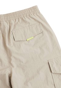 Beige cargo kalhoty mají nařasený pas, dvě boční kapsy, jednu zadní kapsu s žlutým akcentem a texturovanou tkaninu.