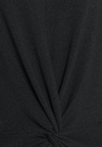 Svart topp med en tvinnad knutdesign vid midjan, tillverkad av texturerad tyg med subtila metalltrådar för visuell intresse.