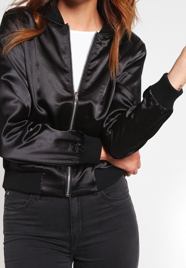 Schwarze Satin-Bomberjacke mit Reißverschluss, gerippten Bündchen und Saum, samt einer glatten Textur und einer figurnahen Silhouette. Kombiniert mit schwarzen Jeans.