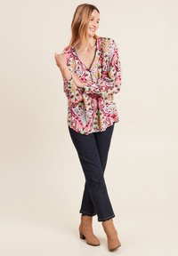 Bluse mit Floralprint in Pink, Grün und Blau, mit tiefem V-Ausschnitt und langen Ärmeln. Kombiniert mit dunkler Jeans und braunen, hohen Stiefeletten.