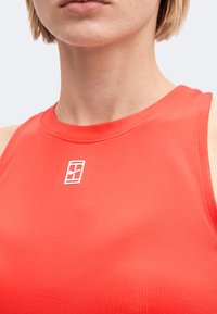 Gros plan d'une personne portant un haut rouge sans manches avec un petit logo Nike blanc sur la poitrine.