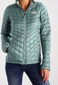 Lehká prošívaná tyrkysová bunda s vysokým límcem a zapínáním na zip po celé délce. Na hrudi má logo, texturovaný vzor a elastické manžety.
