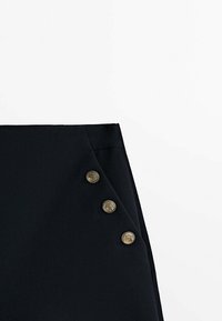 Jupe noire avec un design ajusté, rabat latéral orné de quatre boutons dorés et texture de tissu lisse.