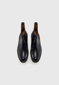 Bottines en cuir noir avec une finition lisse, des détails brogue sur le bout, des panneaux élastiques sur les côtés et des tirants pour un enfilage facile.