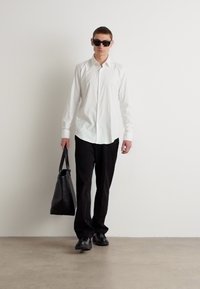 Hvit skjorte med knapper, svarte bukser, svarte sko og solbriller, med en svart tote-veske. Glatt stoff og enkelt design.