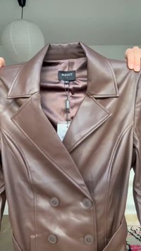 Chaqueta marrón de imitación cuero con doble botonadura, solapas anchas y botones, sostenida por manos, etiqueta con la inscripción "Bardot" talla pequeña.