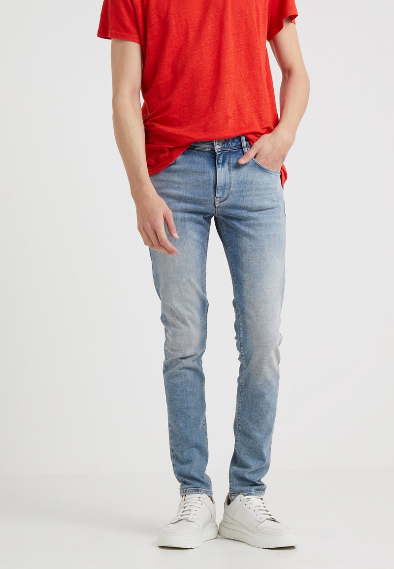 Jeans de mezclilla azul claro con corte ajustado, textura deslavada, bolsillos laterales y cintura regular. Combinados con una camiseta roja y zapatillas blancas.
