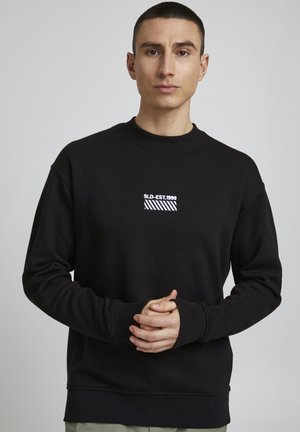 Sort sweatshirt med rund hals, der har et broderet logo på brystet i hvid og diagonale striber. Blødt stof, afslappet pasform.