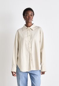 Beige button-up shirt with a collar, long sleeves, and a relaxed fit. Made from textured fabric with a subtle sheen.