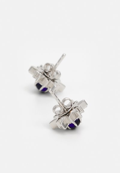 Silver stud earrings feature a floral design with a purple gemstone at the center, complemented by intricate metalwork and a polished finish.