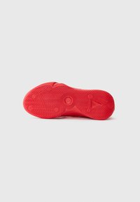 Rød sneakersål med geometriske mønstre og fiskebensmønster synligt mod en hvid baggrund.