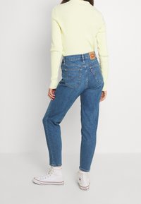 Höga blåjeans av denim har fem fickor, en broderad logotyp på baksidan och är parandes med en ljusgul ribbad tröja.