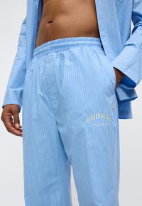 Σετ πιτζάμες ανοιχτού μπλε χρώματος με μικρές ρίγες, κατασκευασμένο από απαλό ύφασμα. Διαθέτει ελαστική μέση και κεντημένο λογότυπο της μάρκας.