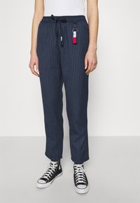 Spodnie w paski w kolorze granatowym z elastycznym paskiem w talii i sznurkiem, z akcentem w postaci breloczka. Połączone z czarnymi wysokimi trampkami.