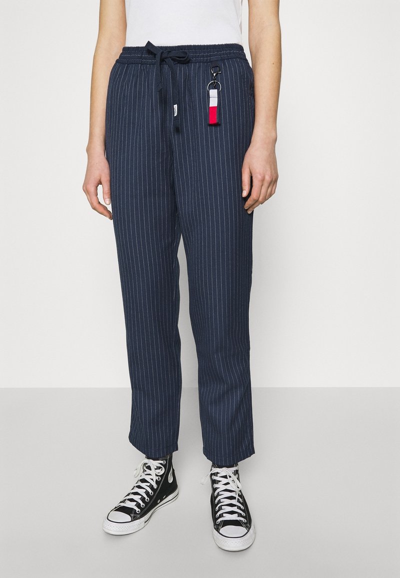 Spodnie w paski w kolorze granatowym z elastycznym paskiem w talii i sznurkiem, z akcentem w postaci breloczka. Połączone z czarnymi wysokimi trampkami.