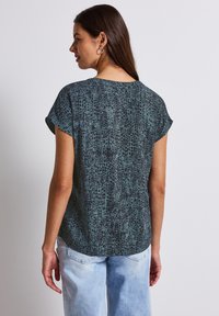 Short-sleeved, dark teal top with a textured, reptile-inspired pattern. Soft fabric, relaxed fit, rounded hem, and invisible stitching.