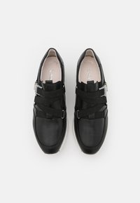 Baskets en cuir noir avec des sangles élastiques, détails en métal argenté, forme de pointe arrondie et semelles rembourrées. Texture lisse et design minimaliste.