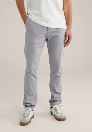 Pantalons en coton gris avec une coupe slim, devant plat et poches arrière, associés à des baskets blanches et gris avec une semelle en caoutchouc.