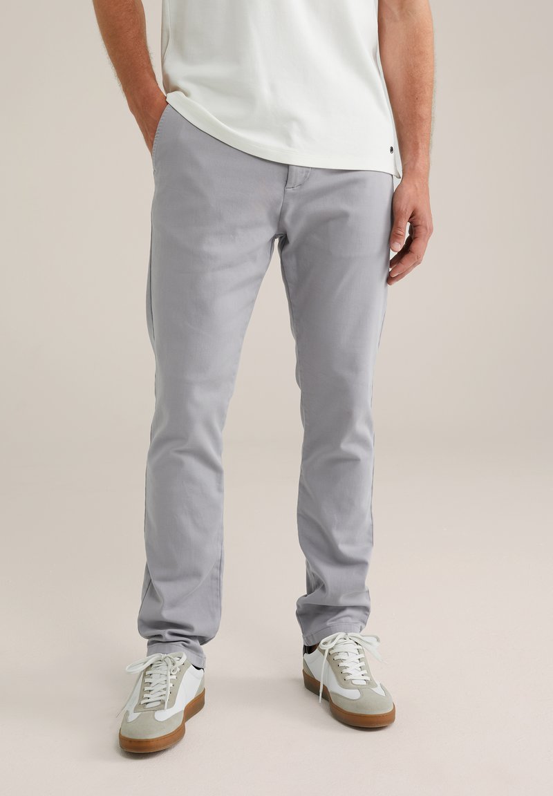 Pantalones de algodón grises con corte slim, frente plano y bolsillos traseros, combinados con zapatillas blancas y grises con suela de goma.