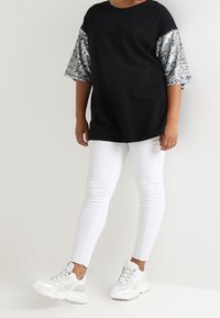 Černé tričko s krátkými rukávy posetými stříbrnými flitry, doplněné o bílé skinny jeans a bílé tenisky. Jednoduchý, ležérní outfit.