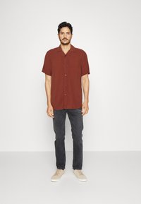 Πουκάμισο με κοντά μανίκια, κουμπωτό, από ύφασμα σε χρώμα σκουριάς με άνετη εφαρμογή, σε συνδυασμό με σκούρα τζιν και μπεζ αθλητικά παπούτσια. Απλός σχεδιασμός, χωρίς σχέδια.