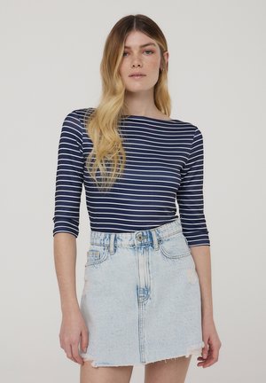 Granatowy pasiasty top z długim rękawem połączony z jasnoniebieską spódnicą dżinsową z postrzępionym dołem i przetarciami, dopasowaną w talii.