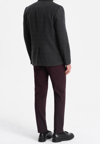 Ciemnoszara kratkowana marynarka z klapami z wcięciem, noszona na bordowych spodniach. Czarne skórzane buty dopełniają strój.