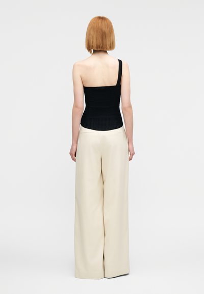 Haut noir côtelé à une épaule associé à un pantalon ample crème taille haute. Tissu lisse et silhouette structurée.