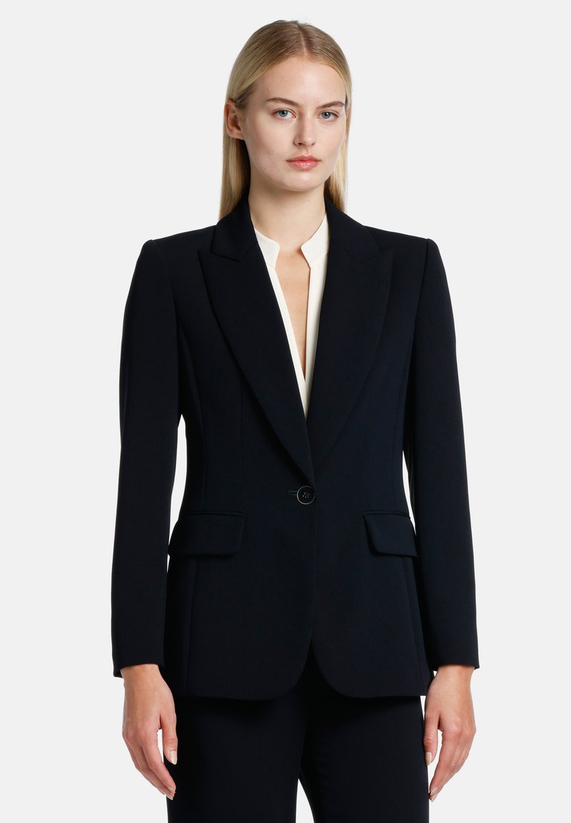 Blazer ajusté bleu marine avec une fermeture à un seul bouton, des revers crantés et deux poches avant. Texture de tissu lisse et silhouette structurée.