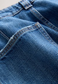 Nahaufnahme von blauen Denim-Jeans, die Gesäßtaschen mit oranger Naht und leicht strukturierter Stoffoberfläche zeigen.
