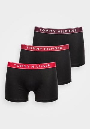 Tres bóxers negros para hombres con cinturillas elásticas de marca en tonos de rojo y burdeos, teñidos con el texto "TOMMY HILFIGER".