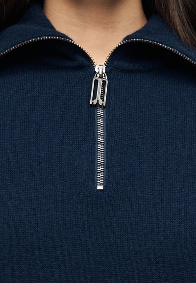Pull à fermeture éclair bleu marine avec une fermeture métallique à double curseur, tissu en maille texturée et col montant pour plus de chaleur.