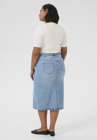 Falda de mezclilla azul clara con una silueta recta, de corte a media longitud y bolsillos traseros. Combinada con una blusa ajustada color crema y bailarinas negras.