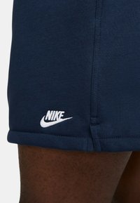 Shorts de sport navy en tissu doux avec un logo Nike brodé en blanc sur l'ourlet. Les caractéristiques incluent un design ajusté et des coutures contrastantes.