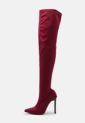 Rödaktig-burgundy lårhög stövel i stretchtyg, med spetsig tå och hög stiletto-klack, med släta sömmar och en jämn yta.