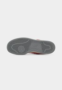 Σόλα ενός γκρι αθλητικού παπουτσιού New Balance με υφή που προσφέρει λαβή και κυκλικό σχέδιο κοντά στα δάχτυλα του ποδιού, τοποθετημένη σε λευκό φόντο.