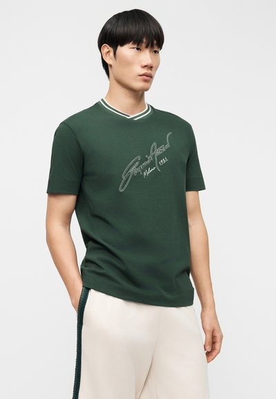 Πράσινο βαμβακερό μπλουζάκι με ριμπ ντεκολτέ που διαθέτει λευκές λεπτομέρειες και κεντητό κείμενο. Κοντά μανίκια και σχέδιο με άνετη εφαρμογή.