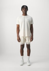 Conjunto deportivo de color beige claro que incluye una camiseta de manga corta y pantalones cortos, fabricado en tejido transpirable, combinado con zapatillas blancas y calcetines.